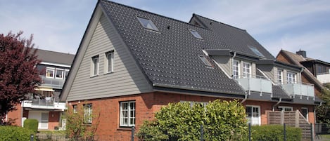 A residential house with a sloped roof, a brick facade, and a fenced yard with yellow flowers.