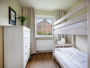 A bedroom with bunk beds, a dresser, a radiator, and a window with a view of a brick building.