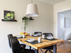 A dining area with a wooden table set for four, black chairs, a hanging plant, and a painting on the wall.