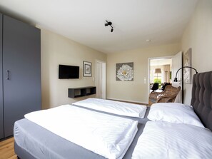 A hotel room with a bed, a TV, a wall-mounted shelf, and a door leading to a balcony.