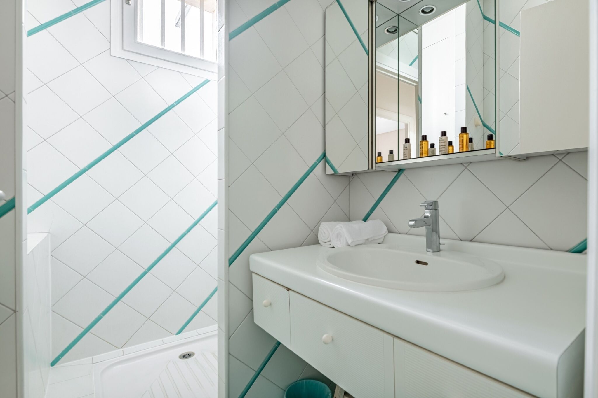 Une salle de bain avec un lavabo blanc, un miroir et une fenêtre.
