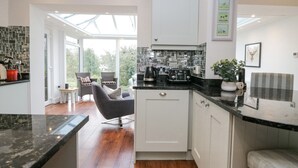 Een moderne keuken met witte kasten, een zwart aanrecht en een eethoek met rieten stoelen.