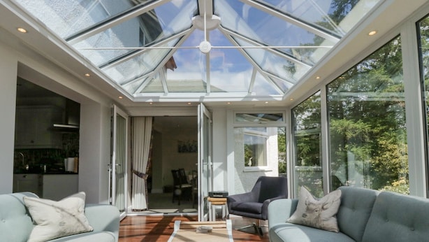 Een moderne woonkamer met een glazen dak, twee banken, een bijzettafeltje en uitzicht op de omgeving.