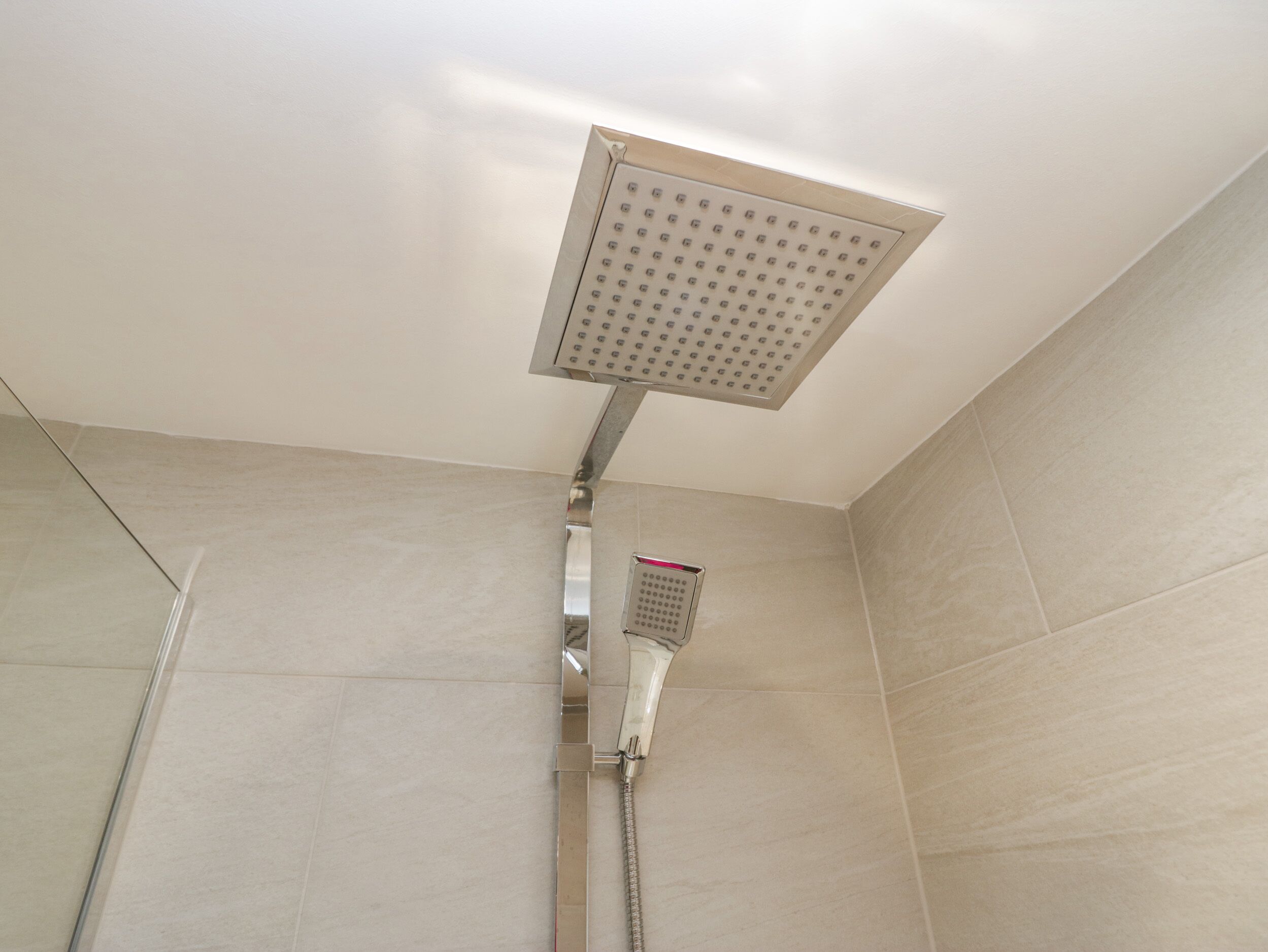 Een douche met een vierkante douchekop bovenin en een handdouche.