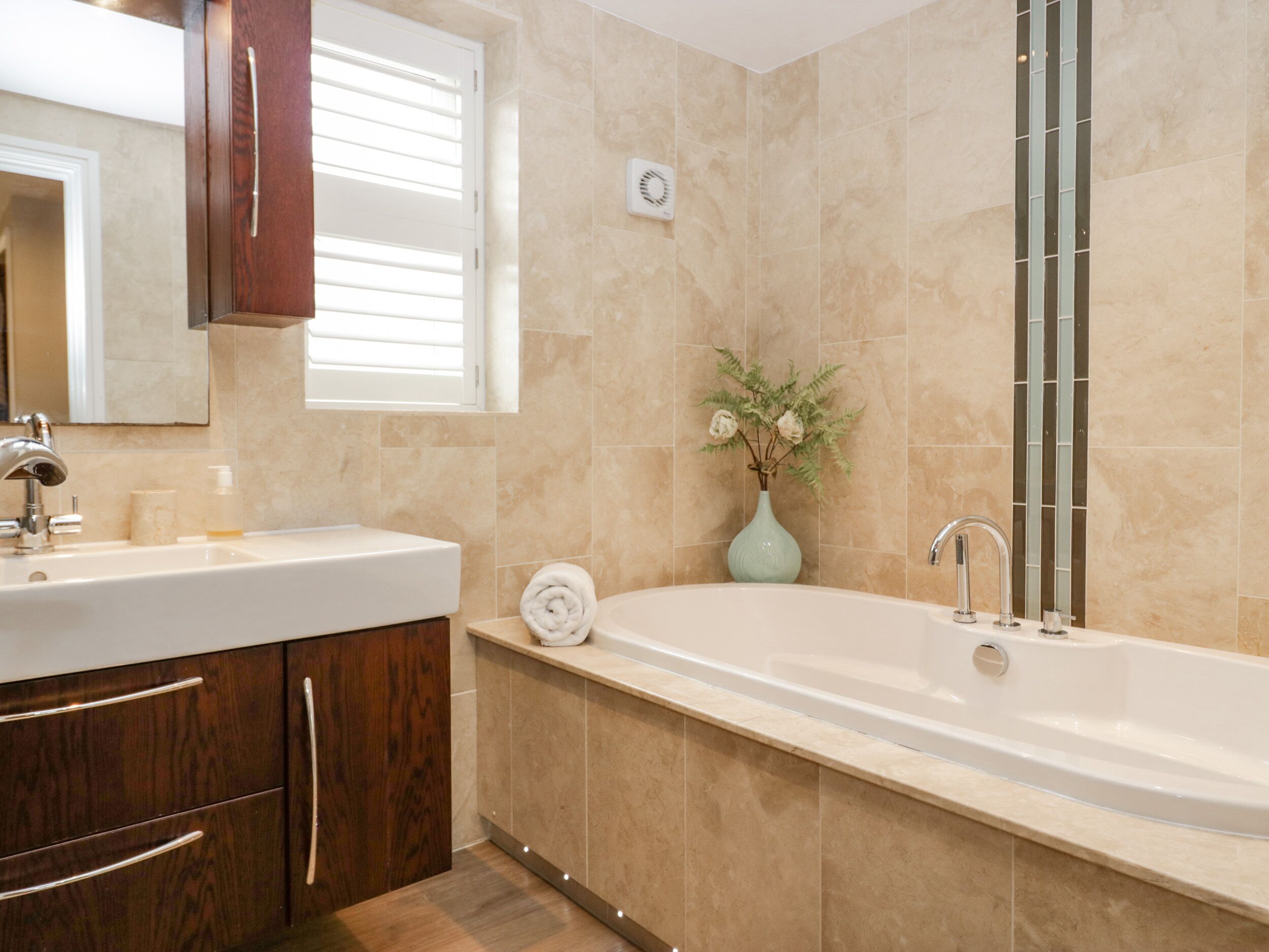 A modern bathroom with a freestanding bathtub, a vanity with a mirror, and a small vase with flowers.
