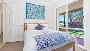 Un dormitorio con un gran ventanal, una cama con ropa de cama blanca, un plaid azul estampada y una obra de arte abstracta azul sobre la cama.
