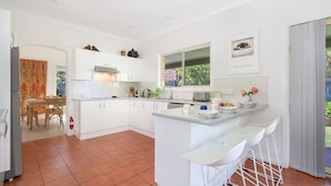 Una cocina moderna con armarios blancos, un comedor con mesa de madera y una pequeña barra con taburetes blancos.