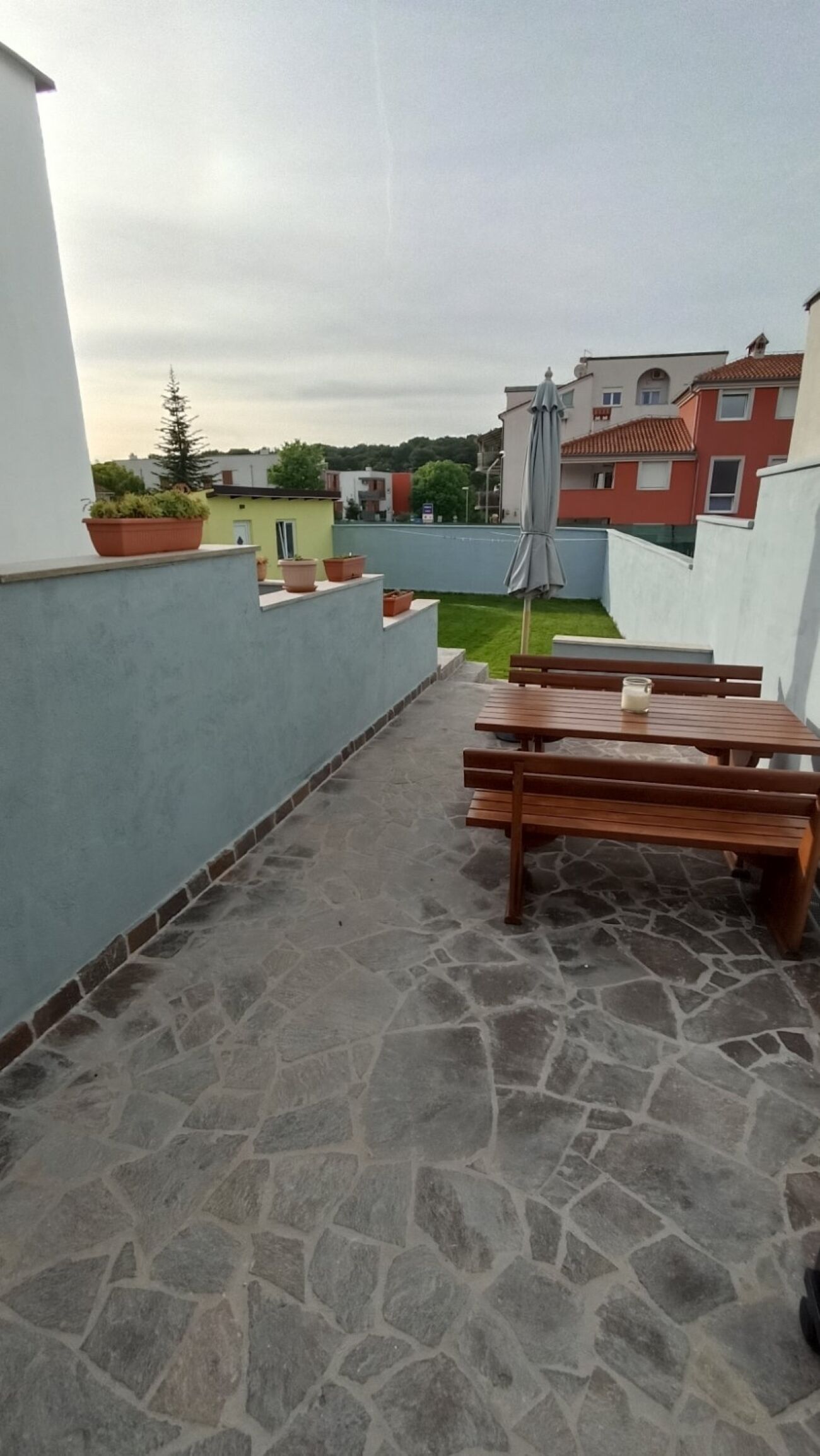 A rooftop terrace with stone flooring, wooden benches, and potted plants.