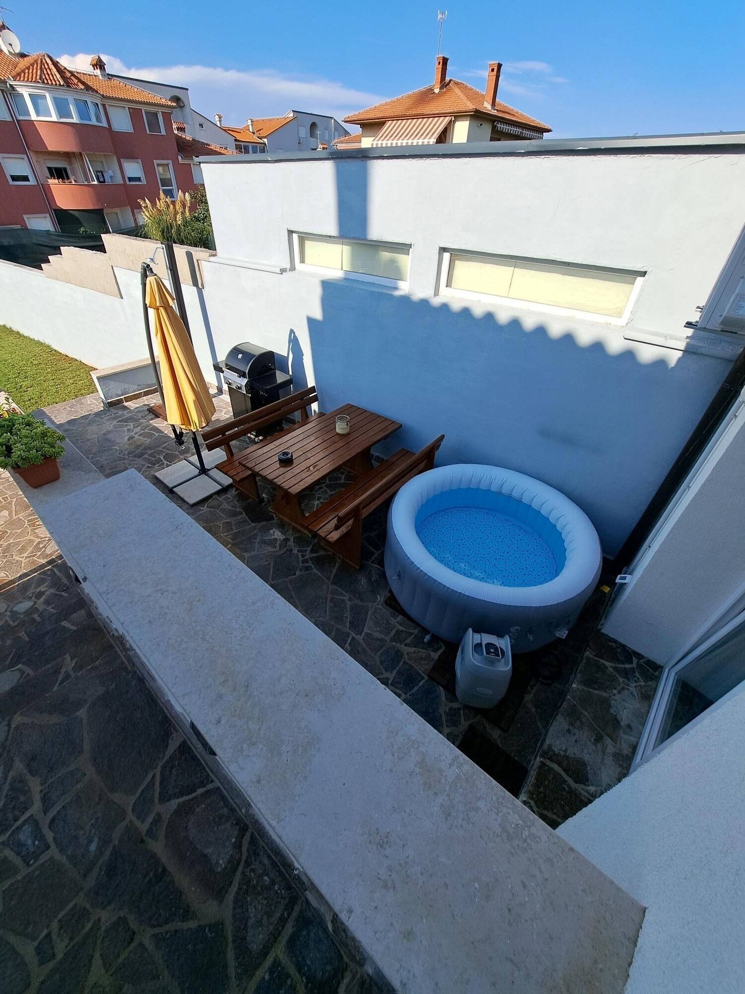 Eine kleine Terrasse im Freien mit Whirlpool, Holztisch und Grill.