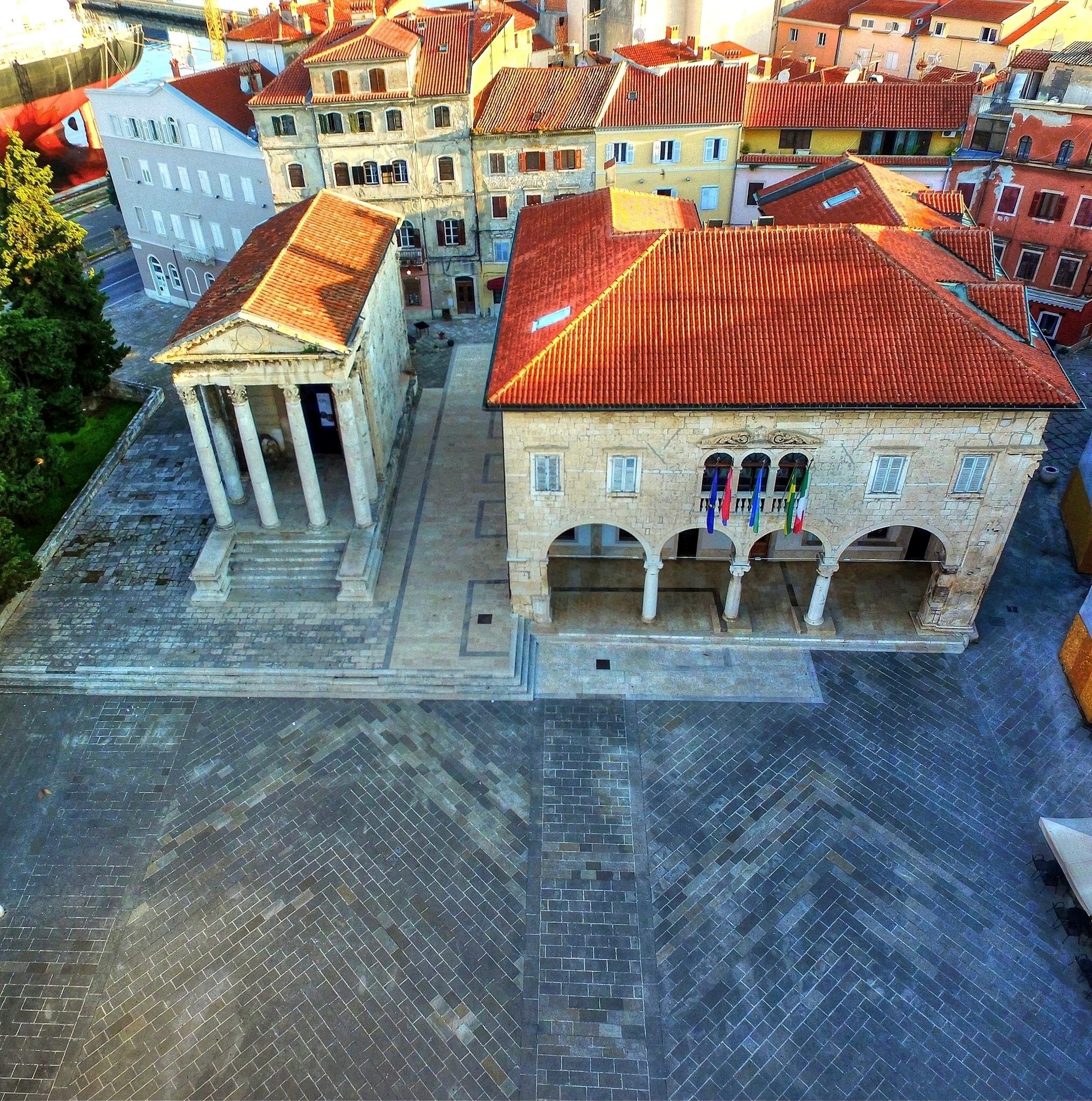 Um edifício histórico com telhado de telhas vermelhas, um pátio central com colunas e uma rua pavimentada à frente.