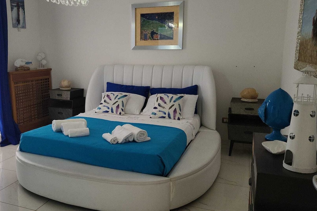 A modern bedroom with a curved bed, white and blue bedding, and a framed picture on the wall.