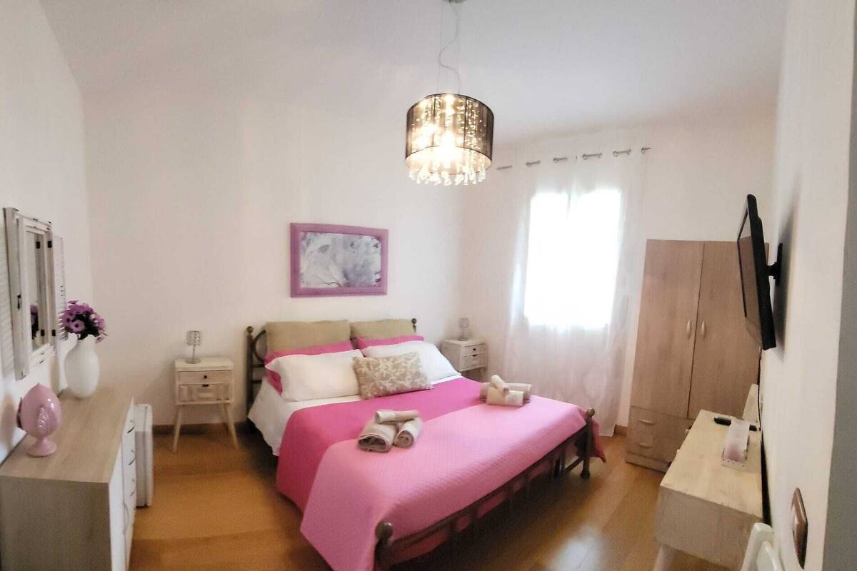 A bedroom with a bed, bedside tables, a dresser, a mirror, a painting, and a window with curtains.
