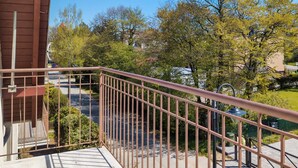 A balcony with a metal railing overlooking a street with trees and parked cars. - Comfortable Studio in Puck | Parking and 400 m to the Beach (Puck)