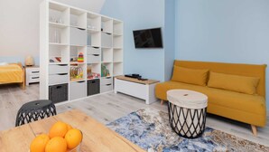 A modern living room with a sofa, a TV, a bookshelf, and a dining area with oranges. - Comfortable Studio in Puck | Parking and 400 m to the Beach (Puck)