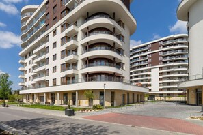 Un immeuble résidentiel à plusieurs étages, doté de balcons, d’une cour aménagée et d’un chemin piétonnier.