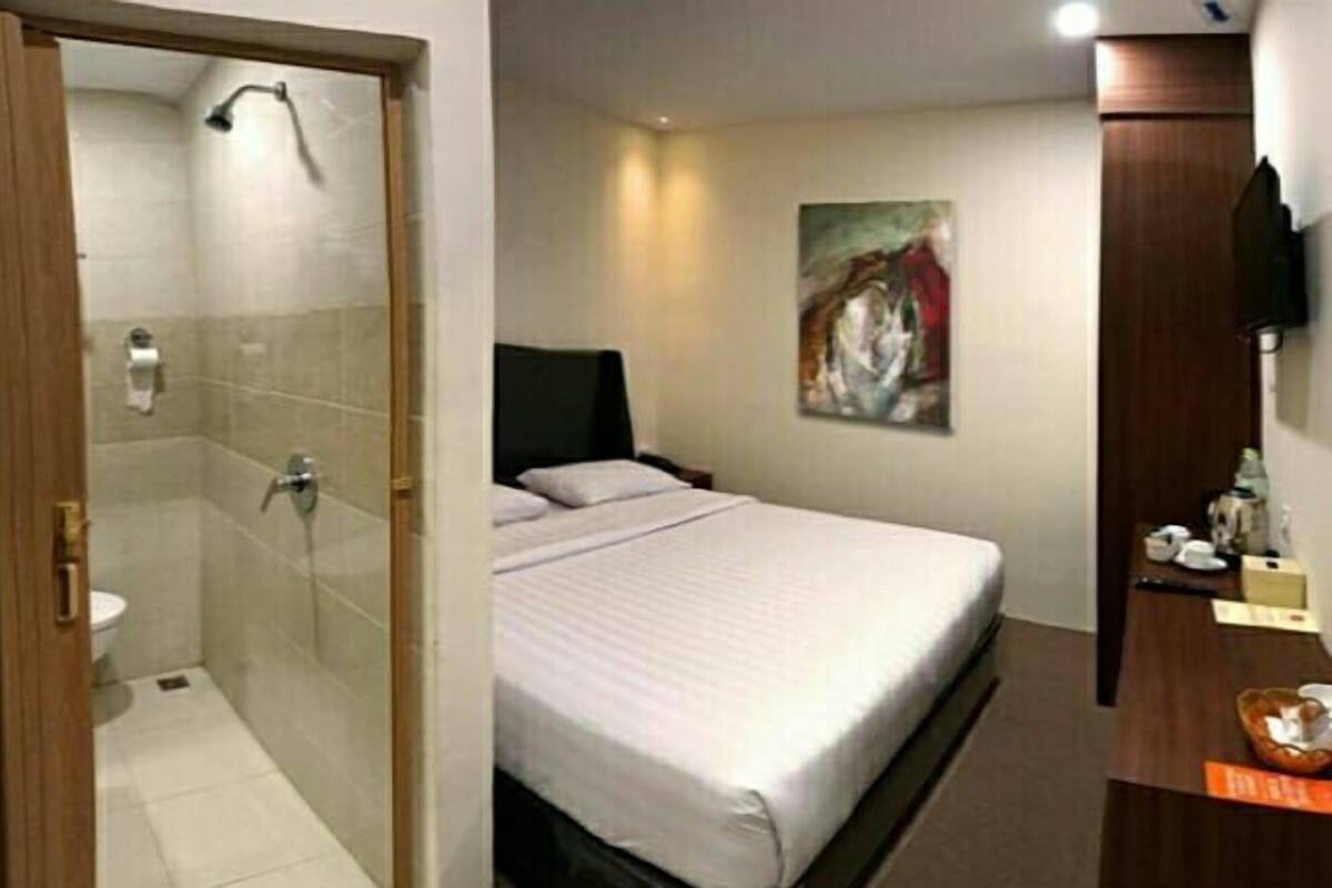 A hotel room with a shower, a bed, a painting on the wall, and a wooden cabinet.