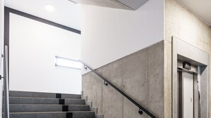 Una escalera con barandilla de metal, pared de concreto y puerta de ascensor.