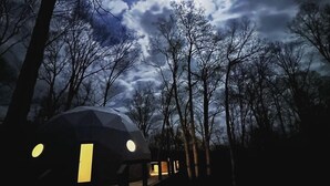 A geodesic dome structure with a circular window and a door, surrounded by trees. - Glamping Dome · Hot Tub, Fire Pit & Forest Views (Simpson)