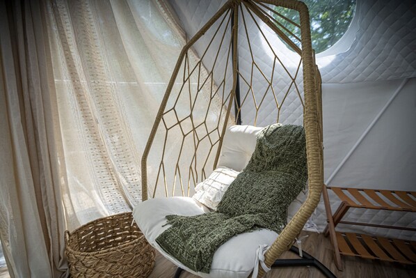 A hanging chair with a woven seat and backrest, a white cushion, and a green throw blanket.