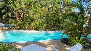 A swimming pool with a white lounge chair in the foreground and lush greenery in the background.