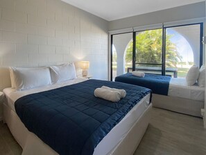 A hotel room with a large bed, a smaller bed, a sofa, a lamp, and a view of the outdoors. - Beachside Palms Unit 3 (Nelly Bay)