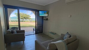 A living room with a sofa, a television, and a view through a glass door to the outdoors.