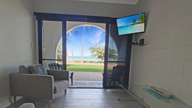 A room with a TV, a sofa, and a view of a beach.