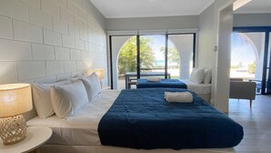 A hotel room with a large bed, a sitting area, and a view through a glass door.