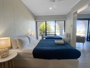 Une chambre d’hôtel dotée d’un grand lit, d’un coin salon et donnant sur l’extérieur grâce à une porte vitrée.