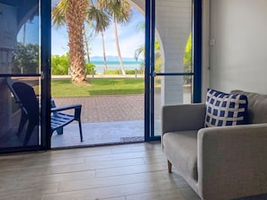 A room with a sliding glass door leading to a patio with a view of palm trees and the ocean.