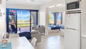 Habitació moderna amb taula de dinar, cadires, sofà i zona de cuina amb nevera, i vista a l'exterior.