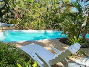 A swimming pool with lounge chairs, surrounded by tropical vegetation. - Beachside Palms Unit 4-BOM (Nelly Bay)