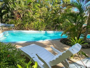 A swimming pool with a white lounge chair in the foreground and lush greenery in the background.