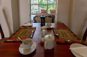 Mesa puesta con platos, tazas y una cafetera, con vista a muebles de exterior a través de una ventana.