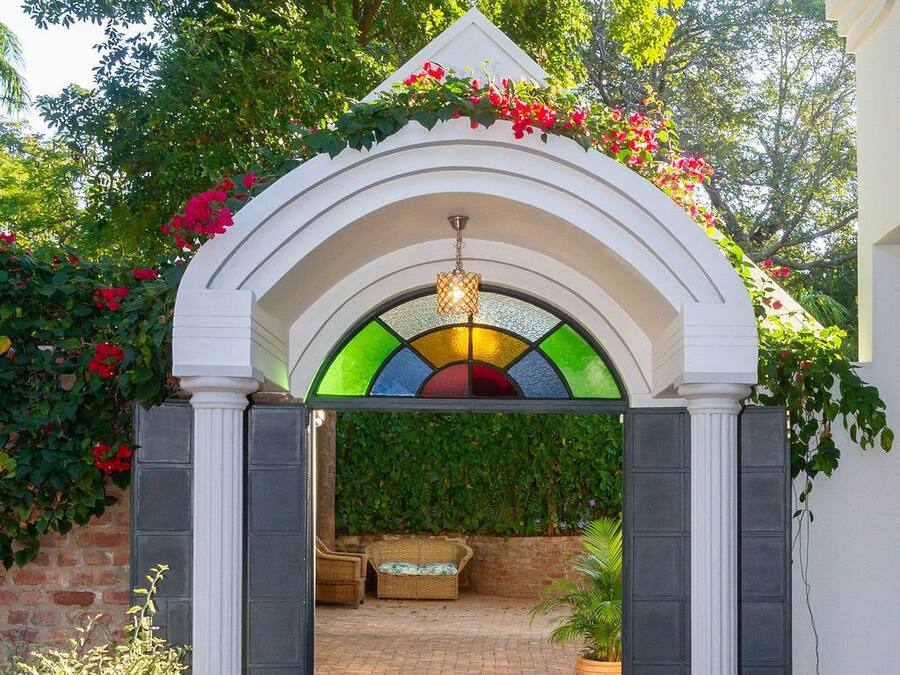 An outdoor covered patio area with a white archway, a wicker sofa, and a potted plant.
