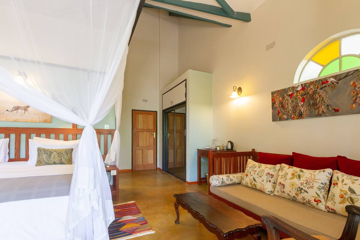 Una habitación con una cama, un sofá, un banco, una mesa y un cuadro en la pared.