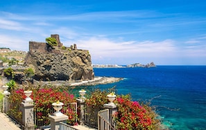 A coastal view with a historic stone structure overlooking the sea, a clear sky, and a distant island.