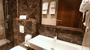 A bathroom with a marble sink, a toilet, a shower, and a mirror. - Monarch Hotel (Prizren)