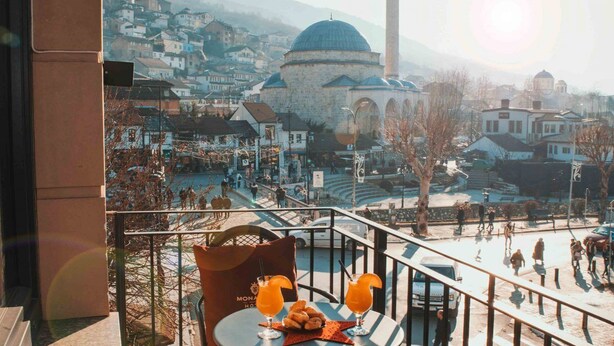 A view from a balcony overlooking a town with historic architecture, including a prominent dome and a minaret. - Monarch Hotel (Prizren)