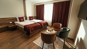 A hotel room with a wooden bed, two pillows, a bedside table with a tray of breakfast, and a TV mounted on the wall. - Monarch Hotel (Prizren)