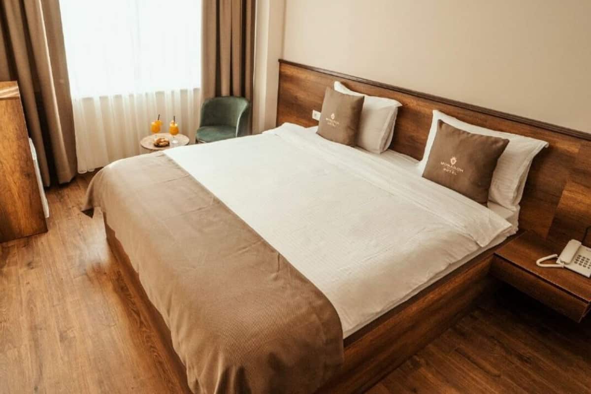 A hotel room with a wooden bed, a bedside table with a phone, and a small table with two candles.