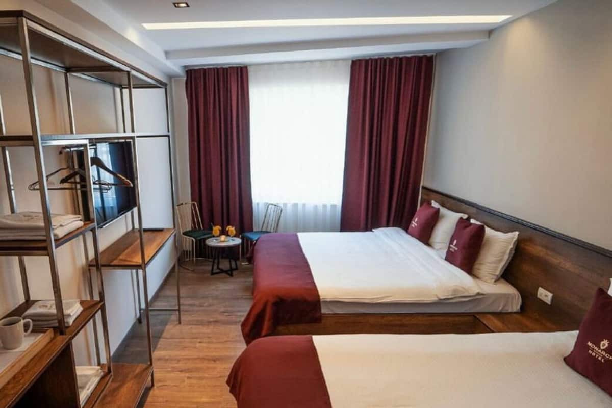 A hotel room with two beds, a desk, a chair, and a TV.