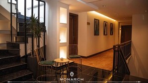 A hotel lobby with a staircase, seating area, and framed artwork on the walls. - Monarch Hotel (Prizren)