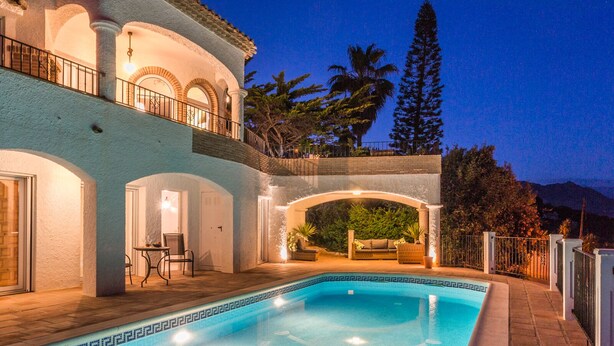 A swimming pool with a geometric tile pattern, surrounded by a white building with arched doorways and a balcony with railing. - Villa with private pool and amazing views (Salobreña)