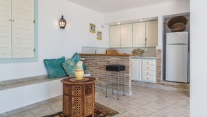 A kitchen with white cabinets, a brick accent wall, a black stool, and a decorative pitcher on a round table. - Villa with private pool and amazing views (Salobreña)