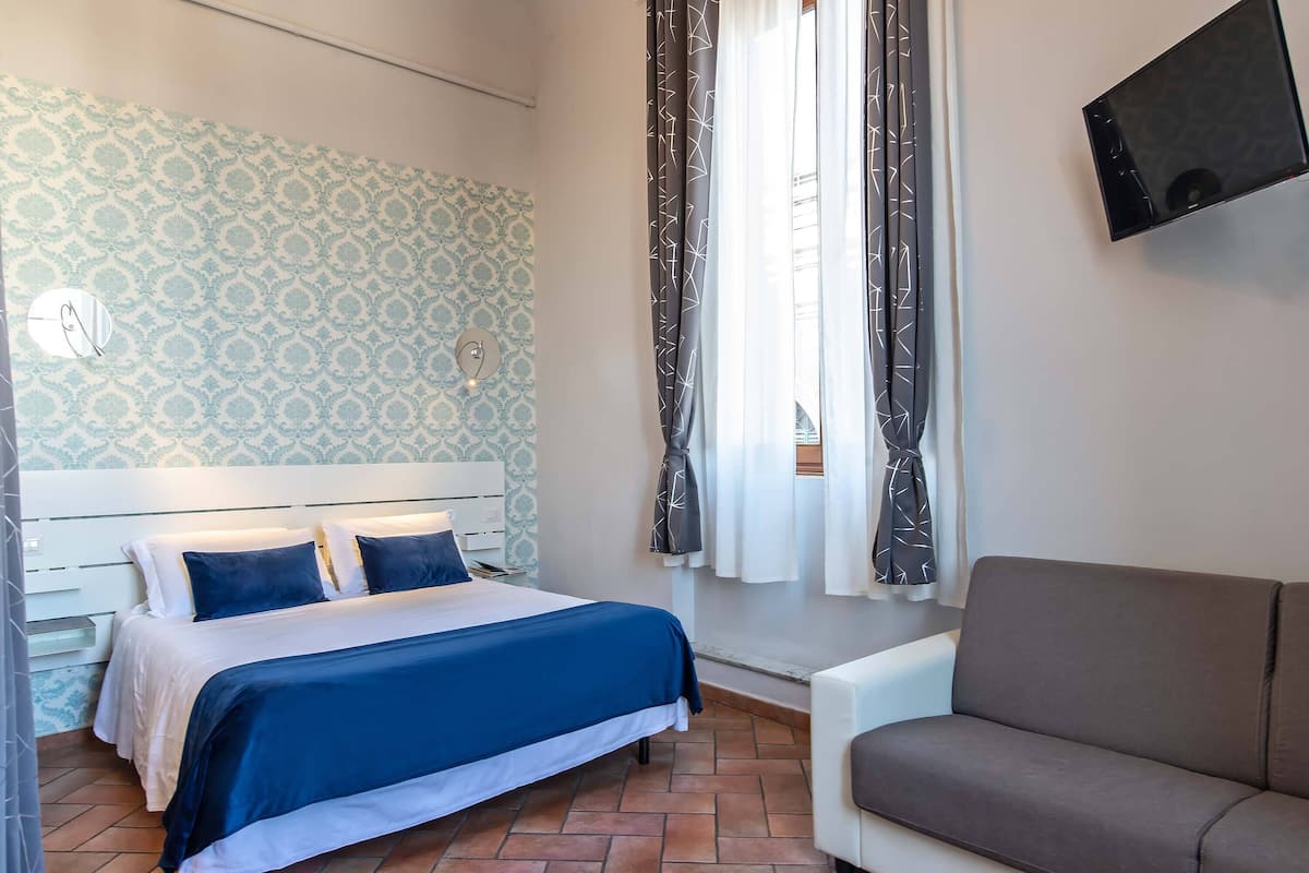 Une chambre à coucher avec un lit, un canapé, une télévision et un papier peint à motifs.