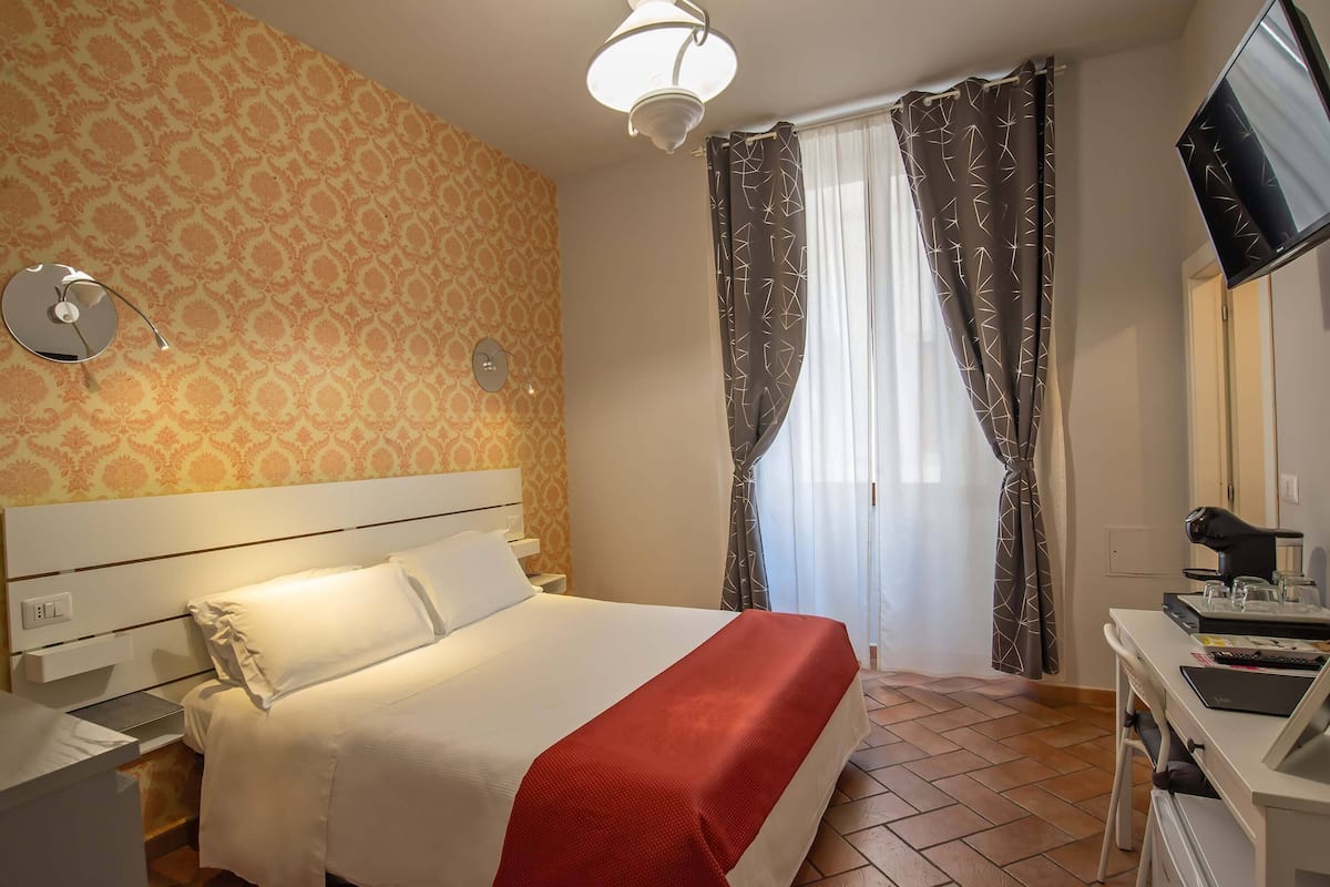 Une chambre d’hôtel avec un lit, un bureau et une chaise, une télévision et des rideaux.