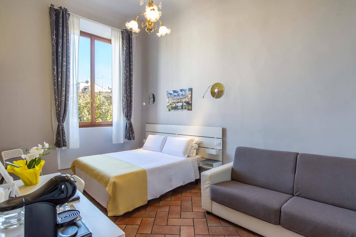 Une chambre d’hôtel comprenant un lit, un canapé, un bureau avec un téléphone et un sèche-cheveux, une fenêtre avec des rideaux et un tableau accroché au mur.