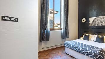 Una habitación oscura con una cama, una ventana con cortinas y vista a la ciudad.