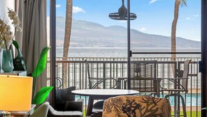 Ein Balkon mit Tisch und Stühlen, einer Hängeleuchte und Blick auf ein Gewässer und Berge.